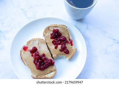 Cup Of Coffee And Peanut Butter Toasts With Berry Jelly On White Marble Table Background In The Kitchen. Making Heakthy Breakfast Process. Top View