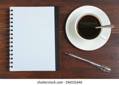 Cup of coffee, pen and opened notepad on desk. Top view