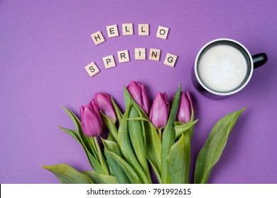 Cup of coffee and Purple tulips on a violet background and wooden letters. Spring concept. Top view, flat lay, copy space