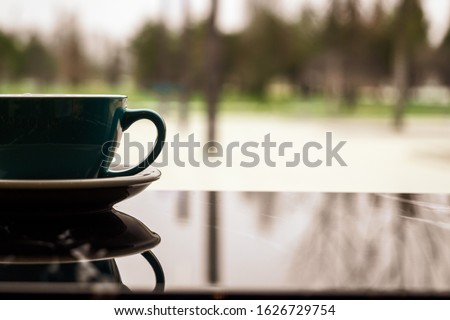 A Cup of coffee with a reflection in a cozy coffee shop. A Cup and saucer stand on a table with a copy space on the background of the window. Warming drink after a walk in cold weather.