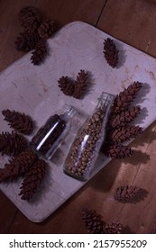Cup of coffee and roasted coffee beans on a marble table surrounded by pine cones. Taken from a top view with a flat layout and dramatic lighting that casts elegant shadows.