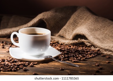 cup of coffee with roasted beans and sackcloth on wooden table
