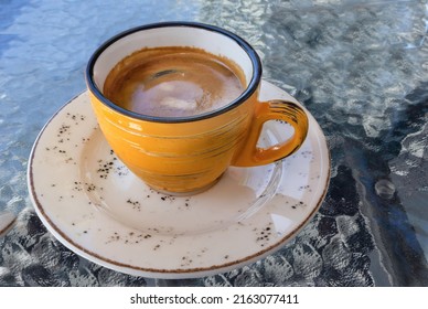 A Cup Of Coffee With A Saucer In An Outdoor Cafe On A Glass Table Surface