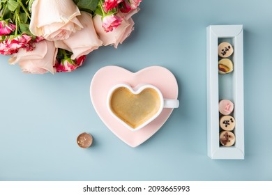 Cup of coffee in shape of heart with chocolate candies and bouquet of roses on blue background. Love concept.  Top view.