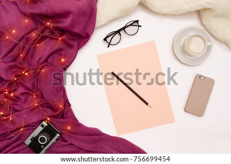 A cup of coffee, smart, pink paper with new years goals. Scarf and Christmas lights on white background.