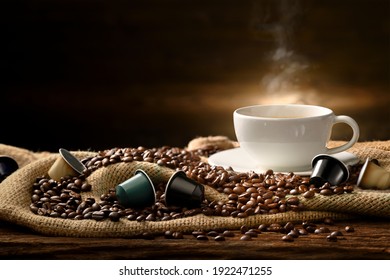 Cup of coffee with smoke and coffee beans and coffee capsules on burlap sack on old wooden background