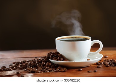 
 Cup of coffee with smoke rising beautifully and coffee beans on a wooden table on dark background.