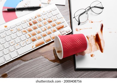 Cup of coffee spilled over computer keyboard on wooden office desk, above view