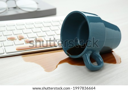 Cup of coffee spilled over computer keyboard on white wooden table