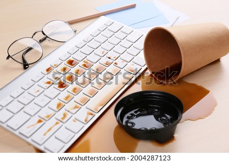 Cup of coffee spilled over computer keyboard on wooden office desk