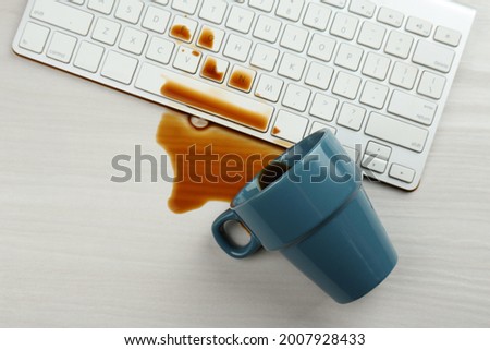 Cup of coffee spilled over computer keyboard on white wooden table, flat lay