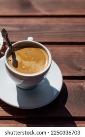 Cup of coffee with spoon on table. White porcelain cup on saucer. Copy space.Black Coffee in natural sun light.espresso on rustic wooden table. good morning concept - Shutterstock ID 2250336703