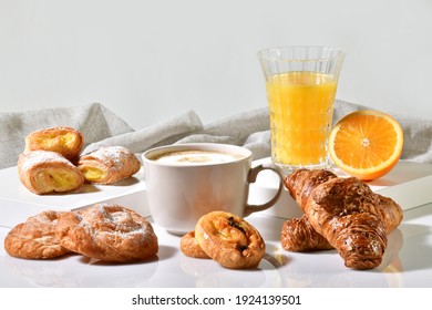 Cup of coffee surrounded by delicious pastries, with an orange juice and half orange at the back on a light background. Traditional breakfast concept.