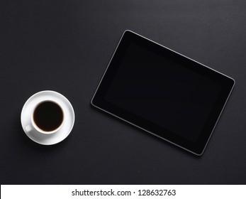 A cup of coffee and a tablet pc over the black background