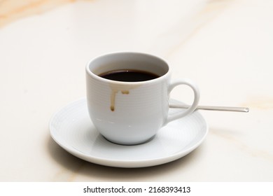 A Cup Of Coffee With Coffee And A Teaspoon On The Saucer, With Some Stains From Having Spilled On A Marble Stone