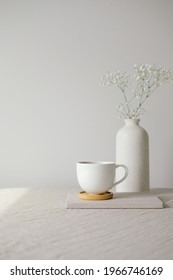 Cup of coffee and vase with gypsophila flowers on table with linen tablecloth. White wall on background. Still life nordic, Scandinavian home decor