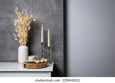 Cup of coffee, vase and other decor on white table near grey wall indoors, space for text. Interior design