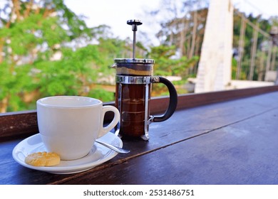 A cup of coffee in a white porcelain cup, a french press filled with coffee, a cookie beside the cup in a table of the cafe near bridge in East Java, Indonesia - Powered by Shutterstock