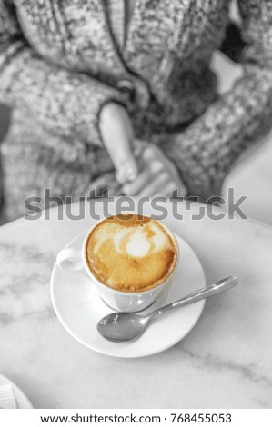 Cup of coffee with woman in knitted coat on the background