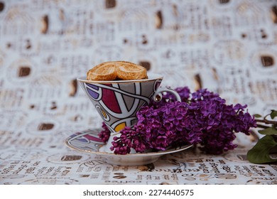 a cup with cookies on the background of a bouquet of lilacs - Shutterstock ID 2274440575