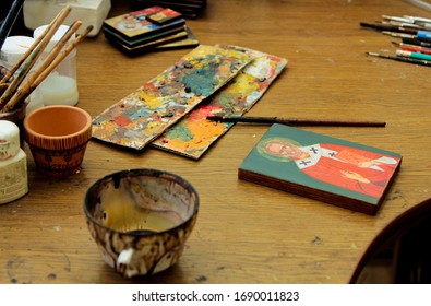 Cup Covered With Paint, With A Wood Stain Substance. Workflow Of The Artist In The Studio. Reproduction Of The Icon Of St. Nicholas. Brushes And Paints On The Background In Studio.