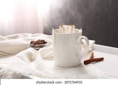 Cup With Drip Coffee Bag And Cinnamon On White Table, Closeup