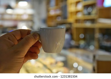 A cup of espresso coffee in hand against the background of a dimly lit cafe