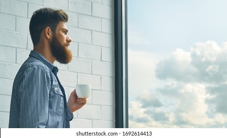 Cup of espresso coffee. Portrait of a bearded young man drinking morning coffee. A bearded man with a mustache looks out the large window.