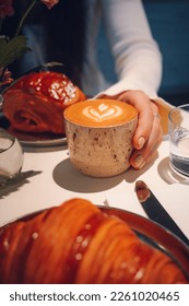Cup of flatwhite coffee in handmade cup on Sunday brunch with Croissant and pain au chocolat in the background, served in the UK