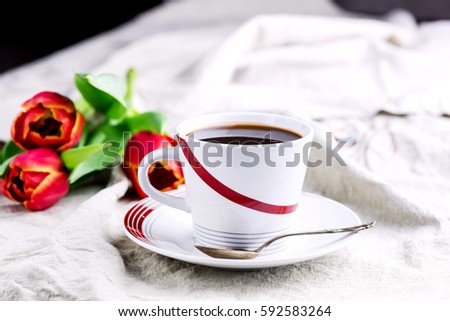 Cup of fresh coffee on linen napkins Three red tulips next to cup Copy space