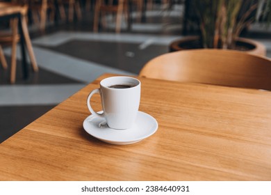 A Cup of freshly brewed black tea at a cafe blurred background. Coffee cup on table cafe shop Interior. Concept of easy breakfast. One white big ceramic cup. Top view. Alternative brewing methods - Shutterstock ID 2384640931