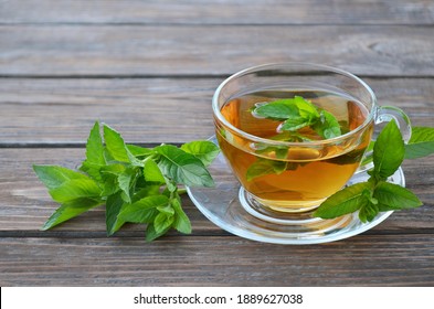 Cup of freshly made hot mint tea with fresh green mint leaves on a old wooden table. Concept of a healthy lifestyle.