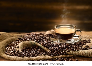 Cup glass of coffee with smoke and coffee beans on burlap sack on old wooden background