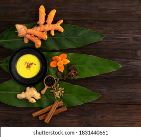 A cup of golden milk,and golden milk ingredients on green turmeric leaf.A plant of the ginger family. Spice and medicinal herb,give yellow colour for food and can help prevent heart disease.