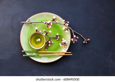 Cup of green tea and peach blossom on dark rustic table as a spring time concept