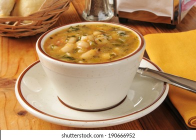 A Cup Of Healthy White Bean And Kale Soup With Dinner Rolls