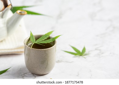 a cup of hemp tea with hemp leaves put on white marble floor