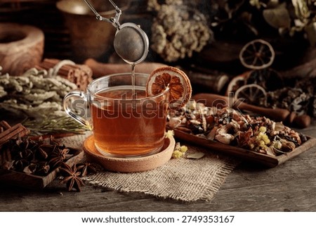 Cup of herbal tea with various dried herbs, flowers, and spices. Tea with ingredients and slices of dried oranges.
