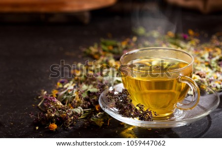 Cup of herbal tea with various herbs on dark background