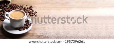 Cup of hot aromatic coffee and roasted beans on wooden table. Space for text