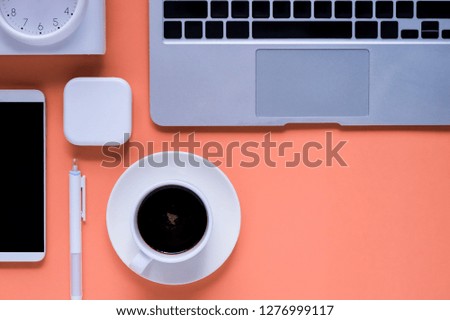 A cup of hot black coffee surrounded by office devices on soft coral tone with copy space at bottom right