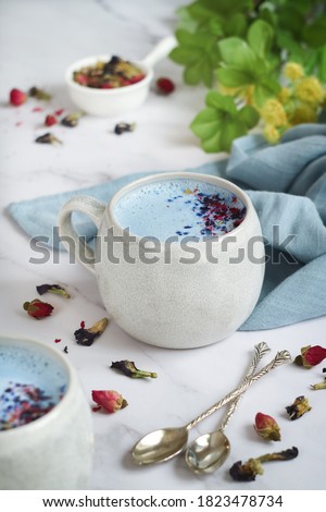 A cup of hot blue moon butterfly milk tea latte with ingredients top with crushed blue pea and rose petals, its caffeine free beverage before bed and an age-old remedy for sleeplessness. 