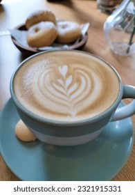 A cup of hot caffe latte served nicely with a touch of latte art. Blue ceramic coffee cup matches perfectly with colours of milk and coffee. Coffee menu in a coffeeshop served with classic donuts.