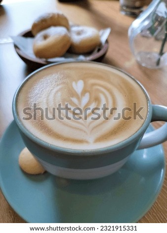 A cup of hot caffe latte served nicely with a touch of latte art. Blue ceramic coffee cup matches perfectly with colours of milk and coffee. Coffee menu in a coffeeshop served with classic donuts.