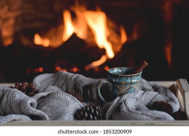 A cup of hot chocolate with cinnamon stick on a tray with warm scarf in front of a fireplace - Powered by Shutterstock