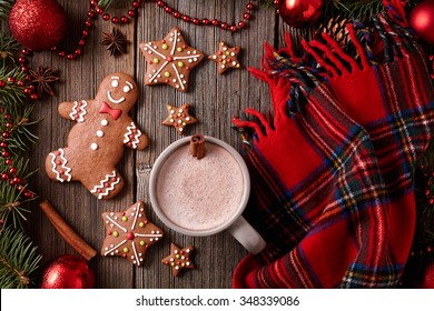 Cup of hot chocolate or cocoa with gingerbread cookies and warm scarf composition in fur tree decorations frame on vintage wooden table background. Homemade traditional food recipe. Top view. Rustic