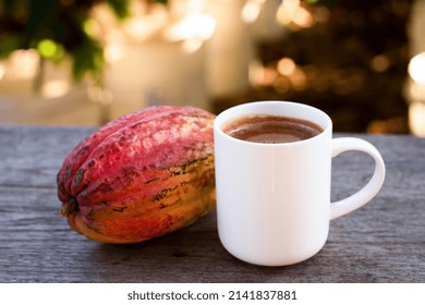 Cup Of Hot Chocolate Drink And Fresh Cocoa Fruit On Wooden Table With Blurred Background.