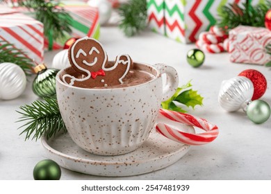 A cup of hot chocolate with a ginger man on top. The ginger man is smiling and wearing a bow tie. The cup is on a white plate and is surrounded by Christmas decorations - Powered by Shutterstock