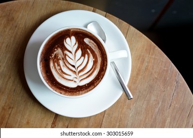 Cup Of Hot Chocolate With Nice Leaf Latte Art And Spoon On Old Wooden Table, View From Above