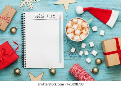 Cup Of Hot Cocoa Or Chocolate With Marshmallow, Holiday Decorations And Notebook With Wish List On Turquoise Vintage Table From Above, Christmas Planning Concept. Flat Lay Style. 